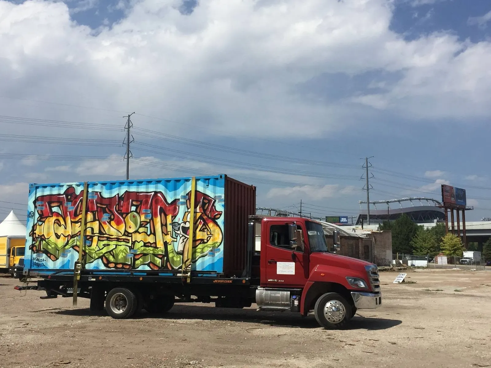 The red Mile High truck carrying a container covered in graffiti, with the stadium behind